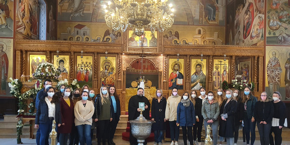 Studierende stehen in einer griechisch-orthodoxen Gemeinde hinter einem Taufbecken