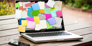 Laptop & Smartphone auf einem Tisch. Der Laptop ist mit bunten Post-Its übersäht. 