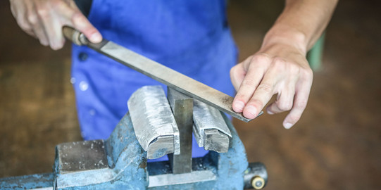 Ein Auszubildender zum Industriemechaniker feilt an einem metallischen Gegenstand.